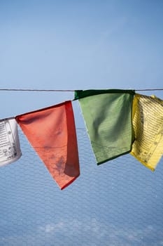 sacred religious multicolored prayer flags on fence moving in the wind showing a bhuddist prayer incantation common in hill stations in Himachal Pradesh India