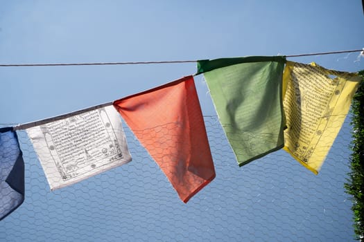 sacred religious multicolored prayer flags on fence moving in the wind showing a bhuddist prayer incantation common in hill stations in Himachal Pradesh India