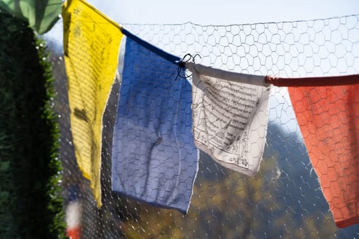 sacred religious multicolored prayer flags on fence moving in the wind showing a bhuddist prayer incantation common in hill stations in Himachal Pradesh India