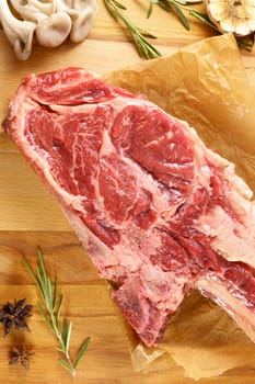 Raw Tomahawk steak on wooden background with spices. Cooking meat. Vertical photo