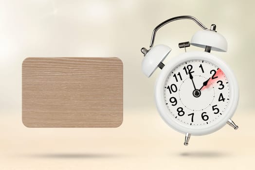 Change time. Winter time concept, on a wooden background. A white alarm clock with a minute hand indicates that the time has been changed to an hour ago with copy space