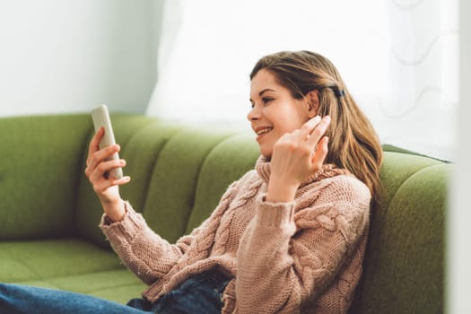 Young caucasian woman with long brown hair in pastel pink sweater and jeans working from home on her laptop and phone. Cheerful woman student studying at home.