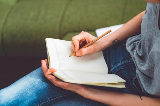 Young caucasian woman with long brown hair in jeans working from home, writing notes. Cheerful woman student studying at home.