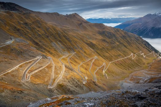 Stelvio pass, mountain road dramatic landscape at dawn above mist, Northern Italy