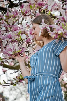 blonde with pleasure inhales an aroman of magnolia flowers standing under a tree. High quality photo