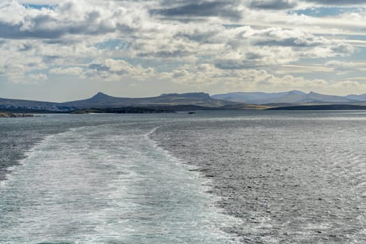 Rugged headlands and rocks as cruise ship departs from port of Stanley on the Falkland Islands