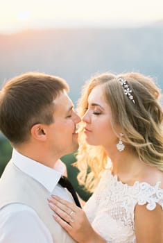 Groom almost kisses bride against the backdrop of mountains. Portrait. High quality photo