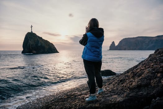Woman travel sea. Happy tourist taking picture outdoors for memories. Woman traveler looks at the edge of the cliff on the sea bay of mountains, sharing travel adventure journey.