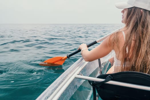 Woman in kayak back view. Happy young woman with long hair floating in transparent kayak on the crystal clear sea. Summer holiday vacation and cheerful female people having fun on the boat.