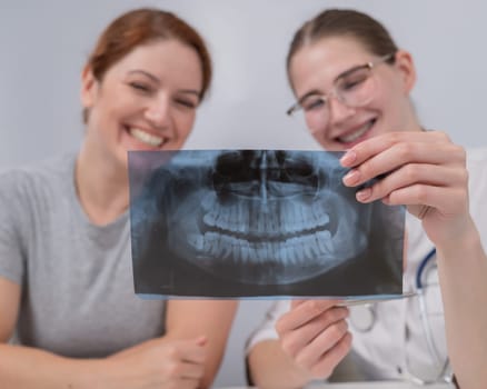 A woman doctor and a patient at the reception are discussing an x-ray of the jaw