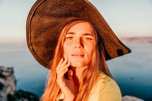 Portrait of happy young woman wearing summer black hat with large brim at beach on sunset. Closeup face of attractive girl with black straw hat. Happy young woman smiling and looking at camera at sea