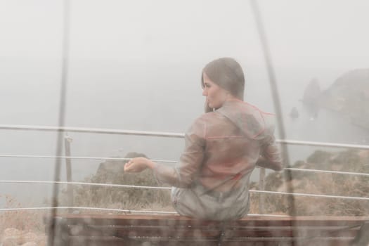 Woman rain park. Happy woman portrait wearing a raincoat with transparent umbrella outdoors on rainy day in park near sea. Girl on the nature on rainy overcast day