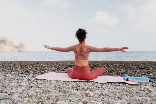 Middle aged well looking woman with black hair doing Pilates with the ring on the yoga mat near the sea on the pebble beach. Female fitness yoga concept. Healthy lifestyle, harmony and meditation.