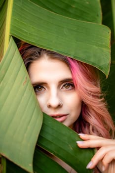 Woman portrait pink hair banana leaf. A beautiful young woman among the huge green leaves of a banana tree