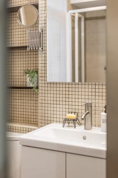 Close-up fragment of stylish bathroom with beige mosaic tiles, mirror, sink and shelves for things. Concept of a comfortable and usable bathroom in a small apartment.