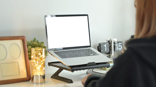 Side view of creative female freelancer sitting in comfortable workplace and working online with laptop computer.