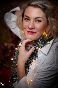 Portrait of a beautiful laughing funny blonde girl with light of garland on dark background before Christmas or New Year