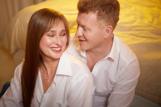 An adult couple of newlyweds in in white shirts in a hotel room after the wedding. A guy and a girl, a man and a woman in beautiful room. The concept of love and care