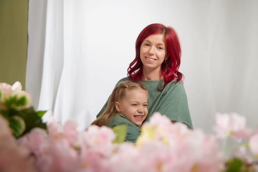 Amazing pretty mother and daughter having fun with flowers in 8 March or in Mother's day. Red haired mom and small little blonde girl having lovely free time on white background in studio