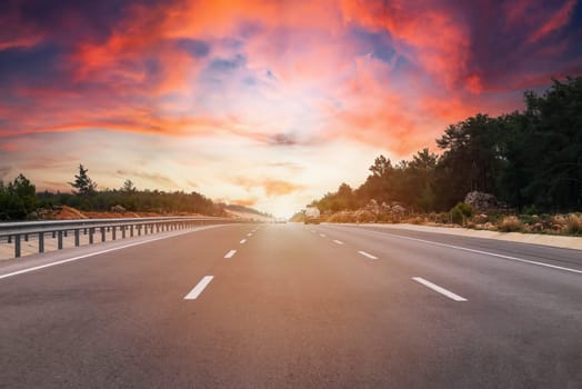 Asphalt road and green forest landscape at sunset