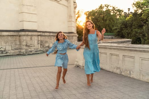 Mother aughter sunset. in blue dresses with flowing long hair against the backdrop of sunset. The woman hugs and presses the girl to her