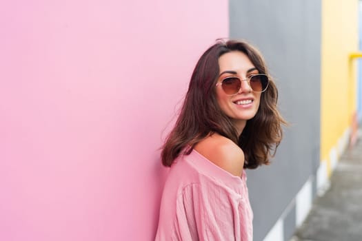 Young beautiful smiling cute romantic woman in trendy summer dress. Carefree woman posing in the street near pink wall. Positive model outdoors in sunglasses. Cheerful and happy.