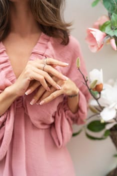 Close shot of romantic cute french gel polish manicure nails. Woman in pink summer dress with flowers around. Rings on fingers. Outdoor shot.