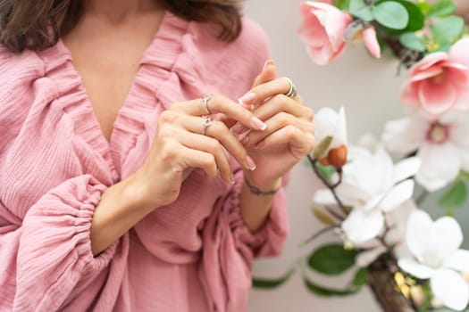 Close shot of romantic cute french gel polish manicure nails. Woman in pink summer dress with flowers around. Rings on fingers. Outdoor shot.