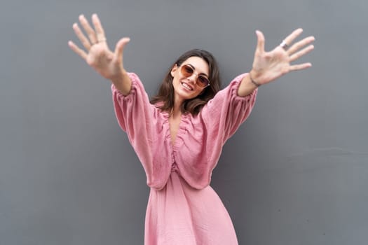 Young beautiful smiling cute romantic woman in trendy summer dress. Carefree woman posing in the street near grey wall. Positive model outdoors in sunglasses. Cheerful and happy.