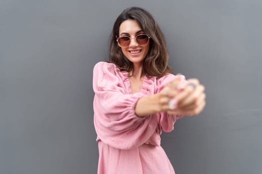 Young beautiful smiling cute romantic woman in trendy summer dress. Carefree woman posing in the street near grey wall. Positive model outdoors in sunglasses. Cheerful and happy.