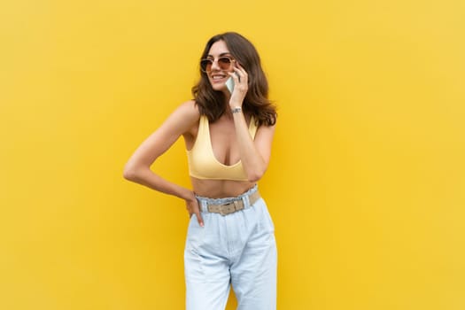 Young beautiful smiling woman with mobile phone. Carefree woman posing in the street near yellow wall. Positive model outdoors in sunglasses. Happy and excited