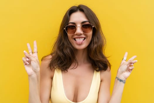 Young beautiful woman. Carefree woman posing in the street near yellow wall. Positive model outdoors in sunglasses. Happy and cheerful showing v sign