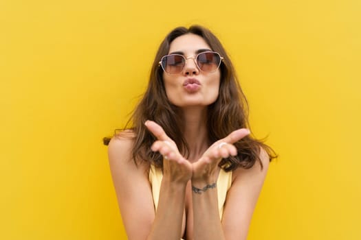 Young beautiful woman. Carefree woman posing in the street near yellow wall. Positive model outdoors in sunglasses. Happy and cheerful send a kiss