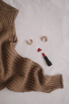 Overhead view of woman's casual outfit with red lipstick and earrings on beige background, Flat lay, top view.