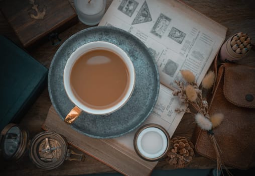 Hot coffee in ceramic cup and brass coffee spoon served with Fresh milk on worktable with old book, brass compass, scented candle and dried flowers. Space for text, Top view, Selective focus.