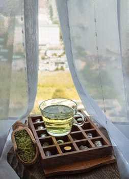Refreshing and Enjoy with A cup of hot hemp tea (CBD herbal tea) and Dried organic hemp leaves on Vintage thimbles collection placed on an Old wooden box on old rustic wooden table by the window view with sunlight. Healthy drink concept. Space for text.