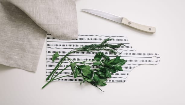 Cutting parsley for salad, top view. Knife slicing greenery on a wooden board on a white background. Preparing organic food, natural healthy homemade eating