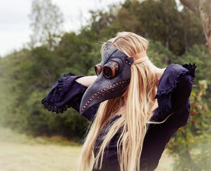 An eerie and surreal photo of a woman in a crow mask standing in a field.