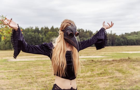 An eerie and surreal photo of a woman in a crow mask standing in a field.