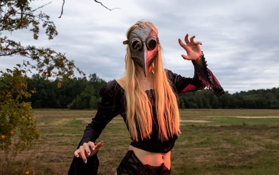 A fascinating and surreal photo of a woman in a crow mask amidst a field and forest.