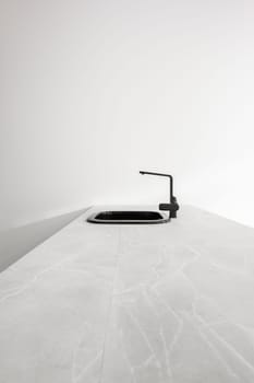Black metal kitchen sink with trendy faucet sits on large white stone kitchen island on light background. Concept of kitchen after renovation or in new building. New plumbing.