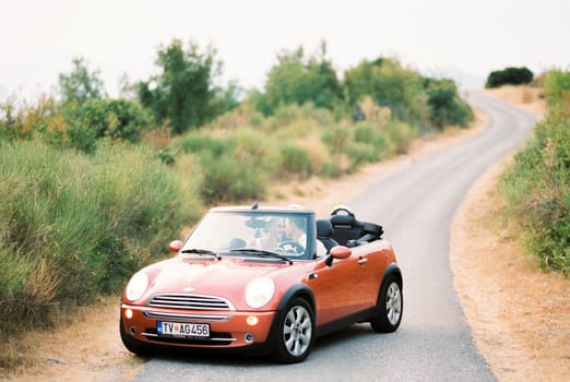 Groom bowed his head to the head of bride, sitting in a convertible on the road. High quality photo