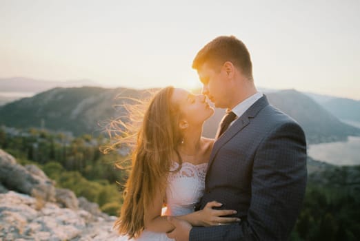 Bride almost kisses groom high in the mountains in the rays of the setting sun. High quality photo