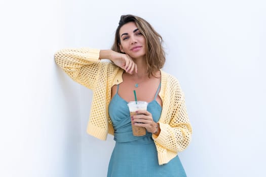 Portrait of beautiful woman in green summer dress on white background natural daylight, holding iced coffee cappuccino happy smiling excited