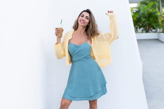 Portrait of beautiful woman in green summer dress on white background natural daylight, holding iced coffee cappuccino happy smiling excited