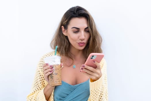 Portrait of beautiful woman in green summer dress on white background natural daylight, holding iced coffee cappuccino and phone thoughtful smiling