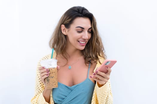 Portrait of beautiful woman in green summer dress on white background natural daylight, holding iced coffee cappuccino and phone thoughtful smiling