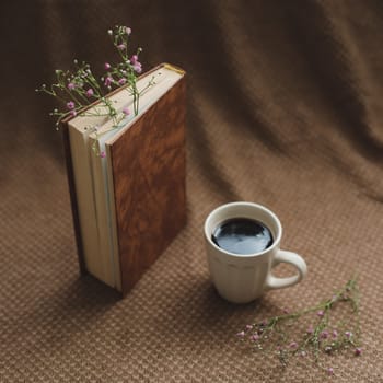 Coffee cup, book, flowers on dark background. Reading, relaxing concept