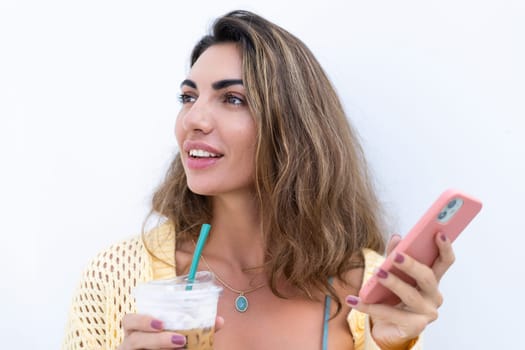 Portrait of beautiful woman in green summer dress on white background natural daylight, holding iced coffee cappuccino and phone thoughtful smiling