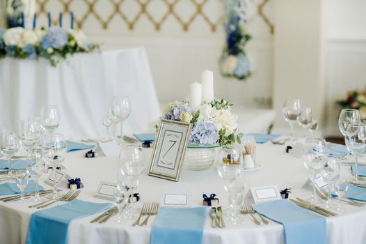 The festive table is decorated in light colors with blue napkins and flowers without food.